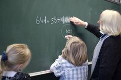 Zwei Kinder und eine Lehrerin vor einer Tafel